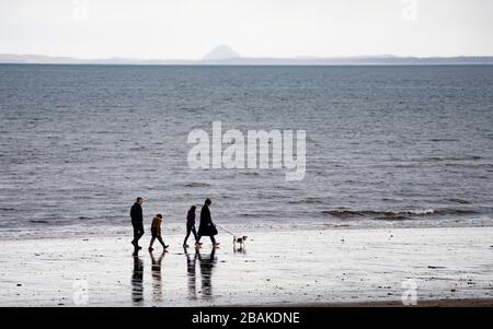 Portobello, Scozia, Regno Unito. 28 marzo 2020. Il primo fine settimana della chiusura dei coronavirus il pubblico era all'aperto esercitandosi e mantenendo le distanze sociali lungo il lungomare di Portobello. Nella foto; Family Walking sulla spiaggia di Portobello, Berwick Law a distanza. Iain Masterton/Alamy Live News Foto Stock