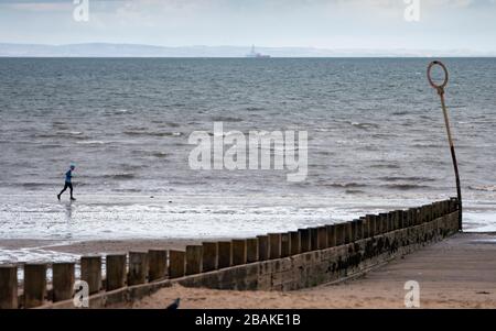 Portobello, Scozia, Regno Unito. 28 marzo 2020. Il primo fine settimana della chiusura dei coronavirus il pubblico era all'aperto esercitandosi e mantenendo le distanze sociali lungo il lungomare di Portobello. Nella foto; Runner sulla spiaggia. Iain Masterton/Alamy Live News Foto Stock