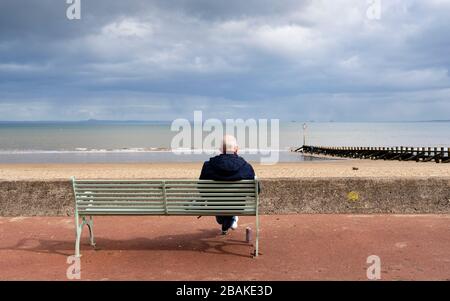 Portobello, Scozia, Regno Unito. 28 marzo 2020. Il primo fine settimana della chiusura dei coronavirus il pubblico era all'aperto esercitandosi e mantenendo le distanze sociali lungo il lungomare di Portobello. Nella foto; uomo solitario su banco che pratica il distanziamento sociale . Iain Masterton/Alamy Live News Foto Stock