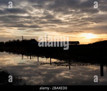 Silhouette di un treno diesel CAF Civity classe 195 gestito da Northern Rail al tramonto sulla linea ferroviaria della costa Cumbria Foto Stock