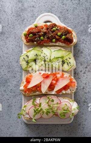 Panini su toast con ingredienti semplici verdure, ravanelli, pomodori, cetrioli decorati microgreens su grigio. Vista dall'alto. Formato verticale. Foto Stock