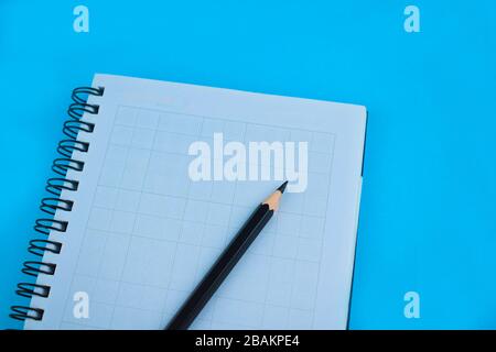 Primo piano immagine di una matita in legno nero pastello su un diario di carta bianca prima di uno sfondo di carta blu Foto Stock