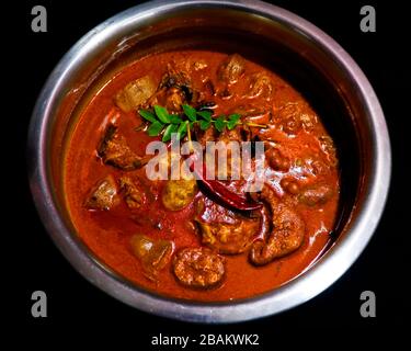 Kerala stile piccante di pesce cocco curry in una pentola di metallo con sfondo nero Foto Stock