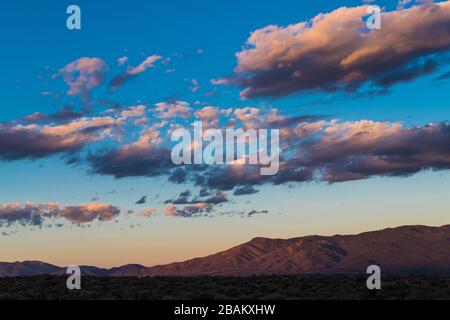 Il bel tramonto illumina le nuvole in sfumature di giallo e viola sopra le montagne Sangre de Cristo vicino a Taos, New Mexico Foto Stock