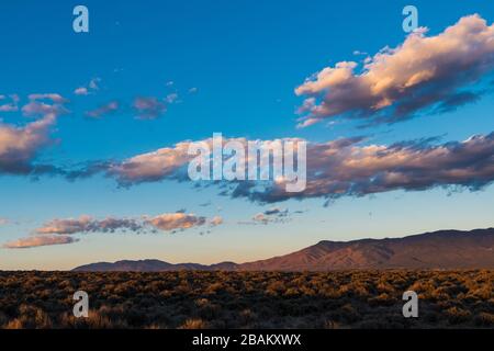 Il bellissimo tramonto irradia colori e sfumature viola e gialle sulle nuvole e sulle montagne Sangre de Cristo vicino a Taos, New Mexico, USA Foto Stock