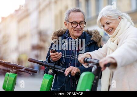 Coppia senior con scooter elettrico e smartphone in città Foto Stock