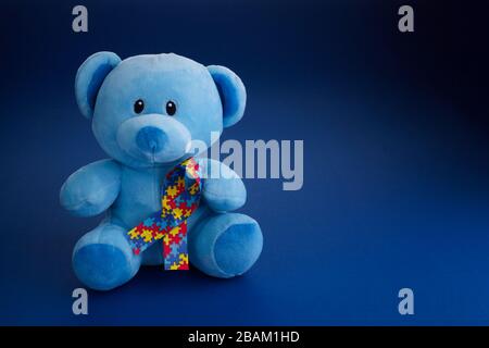 World Autism awareness, concetto con orsacchiotto che tiene puzzle o nastro modello jigsaw su sfondo blu Foto Stock