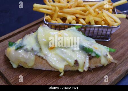 Panino di bistecca di formaggio Philly servito su un pannello di legno con patatine croccanti Foto Stock