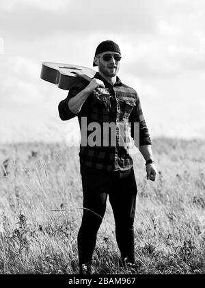 Un musicista in cerca di ispirazione. Ispirando la natura. Uomo bello con la chitarra a contemplare la natura. In cerca di muse. Uniti con la natura. La vacanza estiva. Trasognata wanderer. Atmosfera pacifica. Escursionismo canzone. Foto Stock