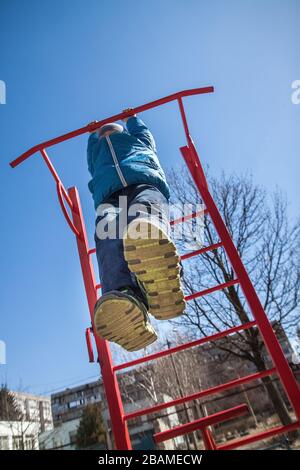 Un bambino ragazzo in una giacca autunno blu e pantaloni jeans gioca su un parco giochi per bambini a Kiev, Ucraina, in una chiara giornata di sole nel cortile di un Foto Stock
