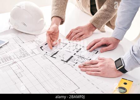 Primo piano di architetti irriconoscibili in piedi alla scrivania e di lavoro con piano casa in ufficio Foto Stock