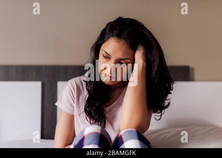 Triste giovane donna seduta da sola a letto in una camera. Concetto di solitudine drammatica, tristezza, depressione, triste. Foto Stock