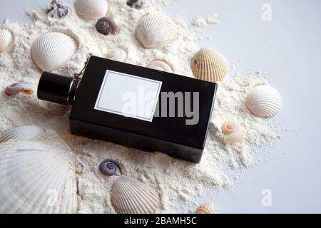 Bottiglia di profumo in vetro nero su sabbia bianca con conchiglie Foto Stock