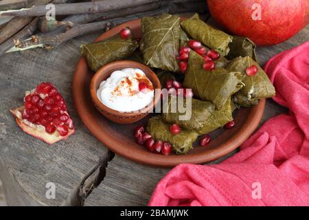 Dolma in un piatto di argilla con melograno, panna acida e chacha su sfondo ligneo Foto Stock