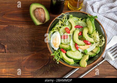 Insalata di cetrioli freschi, foglie di spinaci, rucola, avocado. Servito con fette di uova e pepe rosso. Alimentazione dietetica. Colazione per tutta la famiglia Foto Stock