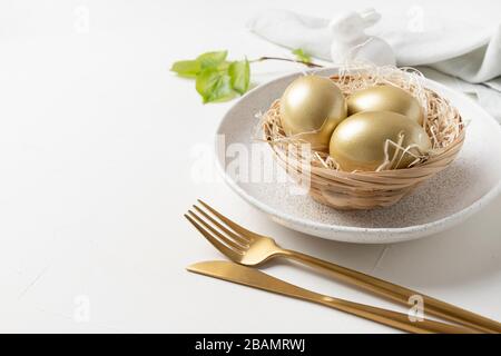 Tavola di Pasqua con coniglietto e uova d'oro su tavola bianca. Spazio per il testo. Primo piano. Foto Stock