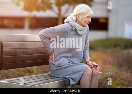 Donna anziana che soffre dal dolore mentre si siede su panchina Foto Stock