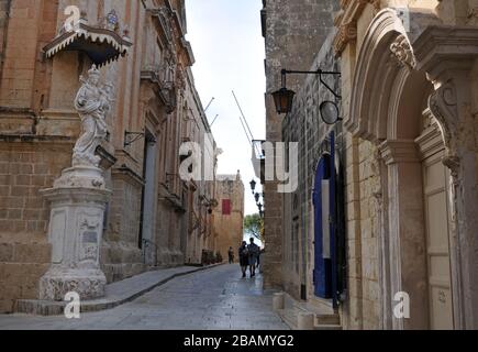 La gente cammina lungo una strada nella storica città murata di Mdina, Malta. Conosciuta come la Città silenziosa, Mdina è una destinazione popolare per i turisti. Foto Stock