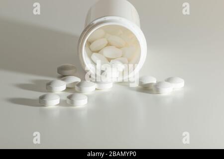 Medicina bianca pila di pillole di prescrizione in una bottiglia bianca su uno sfondo bianco. Foto Stock