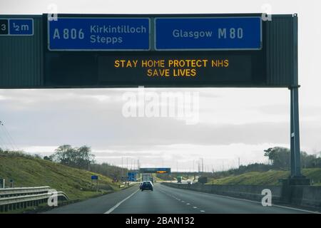 Glasgow, Regno Unito. 28 Marzo 2020. Nella foto: Segnaletica stradale lungo le autostrade M8 e M80 che recita: "STAY HOME PROTECT NHS SAVE LIVES" il Coronavirus Pandemic ha costretto il governo britannico a chiudere tutte le principali città del Regno Unito e a far sì che le persone restino a casa, che ha lasciato le autostrade e tutte le altre strade libere dal solito traffico naso a coda che altrimenti sarebbe lì. Credit: Colin Fisher/Alamy Live News Foto Stock