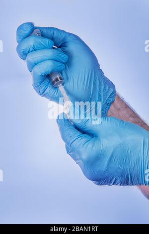 Mani in guanti medici blu che riempiono la siringa con farmaco o vaccino. Su sfondo blu Foto Stock