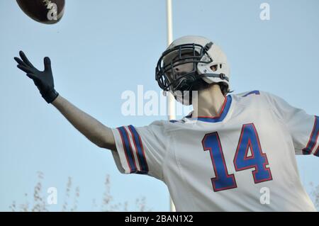 Giocatore che salta a prendere la palla di calcio americana con il cielo come sfondo Foto Stock
