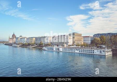 Budapest, Ungheria - 6 novembre 2019: Acqua del Danubio nella capitale ungherese con una nave da crociera turistica enorme. Centro storico in fondo. Nuvole e cielo blu sopra. Foto orizzontale. Foto Stock