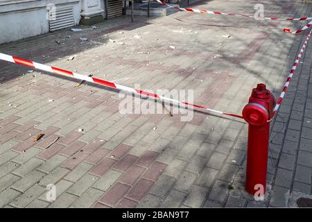 Il nastro di segnalazione rosso bianco racchiude una parte del marciapiede con detriti di costruzione durante la riparazione di un vecchio edificio. Attenzione alla caduta di oggetti. Foto Stock