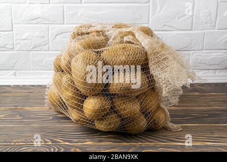 Sacchetto in PP con 10 kg di patate da fattoria. Sacco in rete di polipropilene con 22 libbre di patate biologiche su un pavimento di legno scuro. Acquistare verdure fresche alla rinfusa Foto Stock