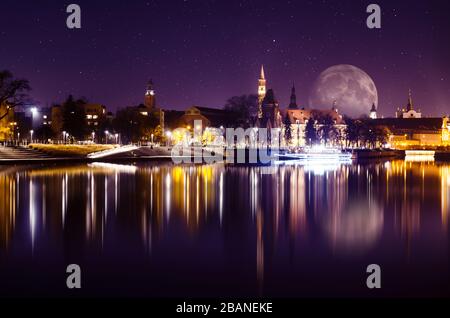 Cielo fantastico con enorme luna sulla città di Wroclaw, il fiume Odra e riflessioni di edifici storici in esso. Sfondo paesaggio urbano. Foto Stock