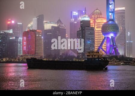 Una nave da carico seduta sul fiume sostenuta dal paesaggio urbano luminoso di Shanghai, Cina. Foto Stock