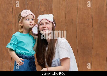 Mamma con una piccola figlia nel sonno maschera sbadiglio e abbracciarsi. Tenere un allarme vicino alla testa. È ora di dormire. Buona notte e buona mattina. Atto mattutino Foto Stock