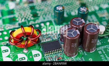 Closeup induttore a nucleo toroidale. Componenti elettronici passivi. Bobina a induzione, microchip, condensatori o resistori sulla scheda di circuito principale del computer verde. Foto Stock