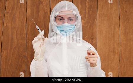 Epidemia di coronavirus cinese. Una donna in tuta protettiva e maschera contiene una siringa per iniezione e un vaccino contro il virus nelle sue mani. Vaccino da c Foto Stock