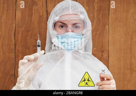 Epidemia di coronavirus cinese. Una donna in tuta protettiva e maschera contiene una siringa per iniezione e un vaccino contro il virus nelle sue mani. Vaccino da c Foto Stock