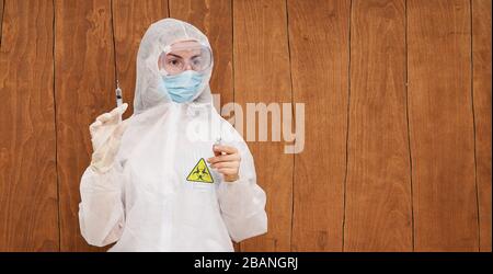Epidemia di coronavirus cinese. Una donna in tuta protettiva e maschera contiene una siringa per iniezione e un vaccino contro il virus nelle sue mani. Vaccino da c Foto Stock