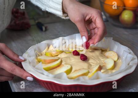 La padrona di casa sta preparando la mela charlotte in cucina. Mette il bacche su una torta di mele in un piatto da forno. Pasta di mele cruda Foto Stock