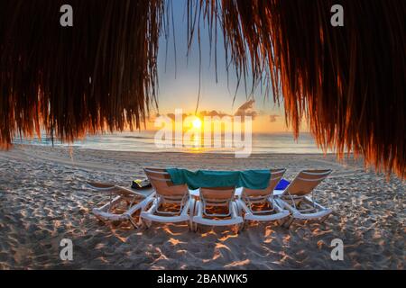 Bella alba dorata su una spiaggia vuota e fila di sedie a sdraio sulla costa caraibica del Messico a Riviera Maya a Cancun, vista da dietro Foto Stock