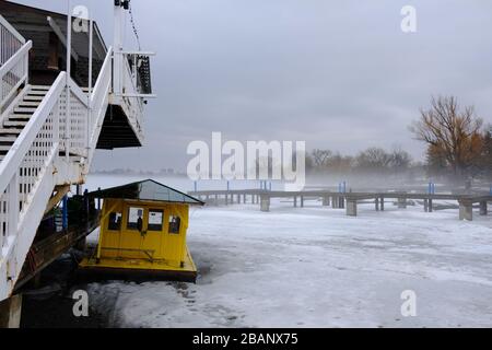 Una fitta nebbia sorge da un lago di Dow's ghiacciato in una calda mattina primaverile, oscurando il molo e l'arboreto alle spalle. Ottawa, Ontario, Canada. Foto Stock