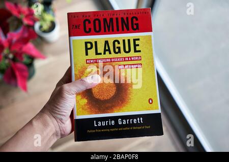 Mano che tiene il libro 'la peste imminente: Nuove malattie emergenti in un mondo fuori equilibrio' da Laurie Garrett, pubblicato per la prima volta nel 1994. Foto Stock