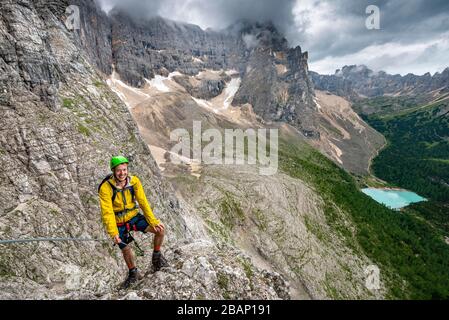 Giovane uomo, alpinista su corda fissa, Via Ferrata Vanelli, vista sul Lago di Sorapis, circuito Sorapiss, montagne con nuvole basse, Dolomiti Foto Stock