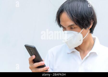 Un uomo asiatico indossa la maschera N95 e usa lo smartphone Foto Stock