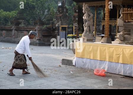 Il dipendente del tempio vestito con abiti tradizionali balinesi, che spazzano il cortile interno pulito prima che i fedeli arrivino a pregare a Tirta Empul. Foto Stock