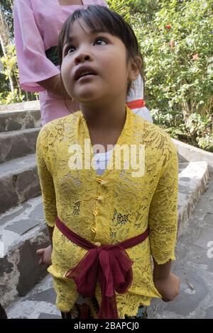 Giovane ragazza balinese in giallo brillante con cintura rossa a guinzaglio guardando la Madre su gradini del Tempio Hindu. Foto Stock