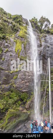 MILFORD SOUND, NUOVA ZELANDA - 21 novembre 2019: Cascata e turisti sul ponte passeggeri nave tiro da sotto, girato in chiaro nuvoloso ligh Foto Stock