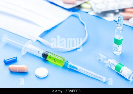 Pillole, siringa, vaccino e maschera respiratoria come un concetto di coronavirus. Maschera protettiva facciale, pillole e pillole, siringa con vaccino su un dorso blu Foto Stock