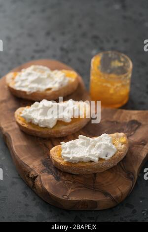 Fette di ciabatta con marmellata d'arancia e ricotta su tavola d'oliva Foto Stock