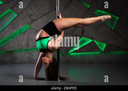 Bella ragazza che fa acrobatici e trucchi flessibili sulla pole in studio di danza Foto Stock