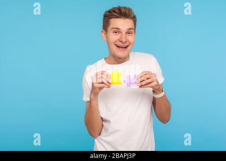 Uomo divertente positivo in t-shirt bianca con due parti di puzzle e sorridente gioiosamente, pronto a collegare i pezzi di puzzle, simbolo di Unione e associazione. In Foto Stock