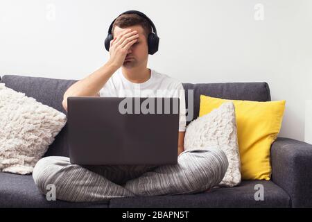 Giovane frustrato seduto sul divano con il portatile. Foto Stock